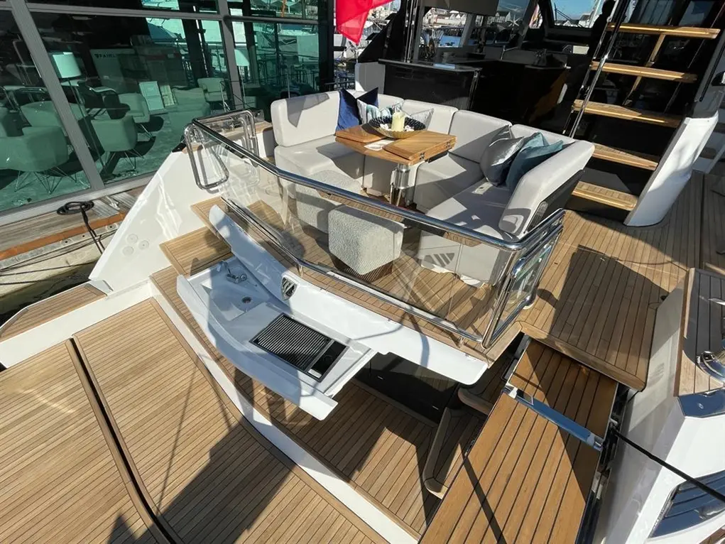 A luxury yacht's deck with a glass railing, seating area, wooden flooring, and a small table set for dining.